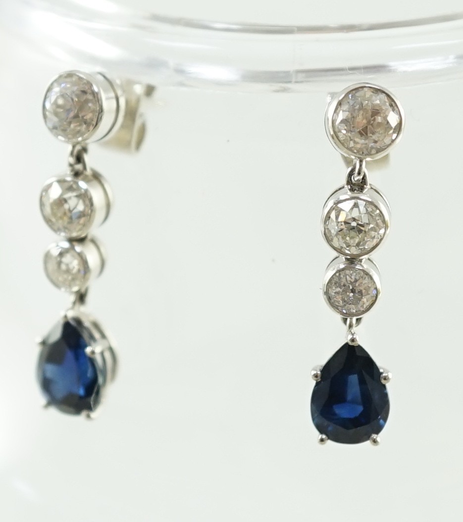 A pair of 1980's platinum, single stone pear cut sapphire and graduated three stone collet set diamond drop earrings